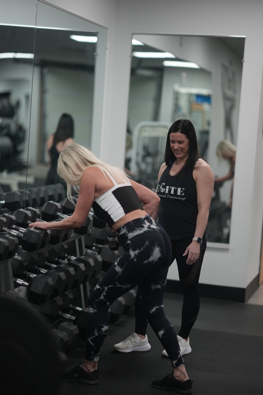 Female personal trainer smiling while training client on dumbbell rows in a gym. Female personal trainer smiling while training client on dumbbell rows in a gym.